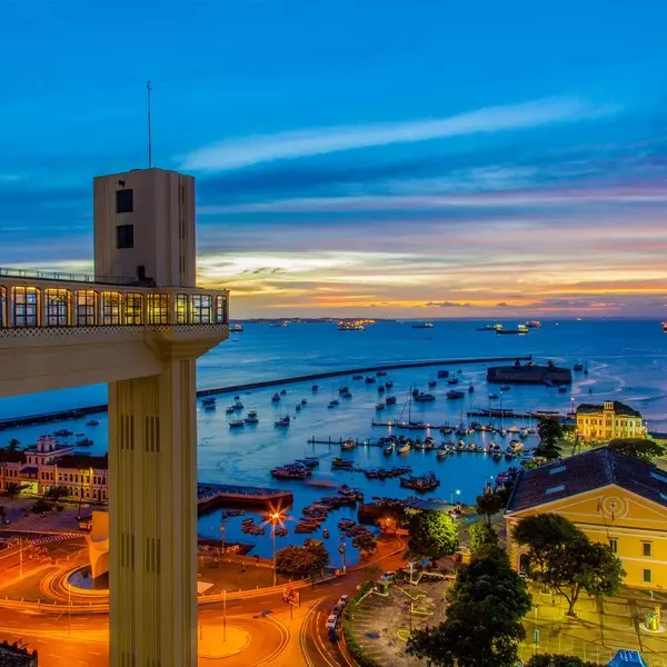 Torre do elevador Lacerda a frente da cidade baixa de Salvador,  capital da Bahia com o Mercado Modelo em segundo plano junto do mar e vários barquinhos.