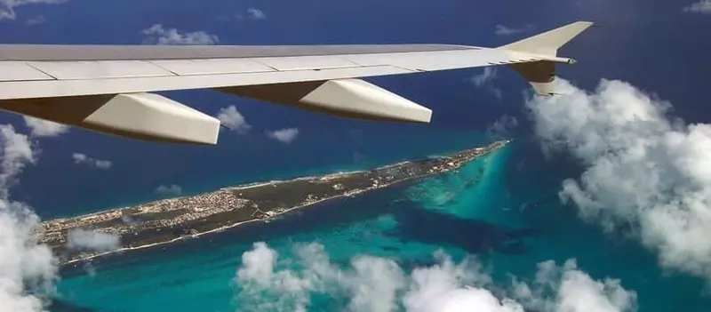 Asa de um avião acima de uma região de Cancún, cercada pelo mar azul do Caribe