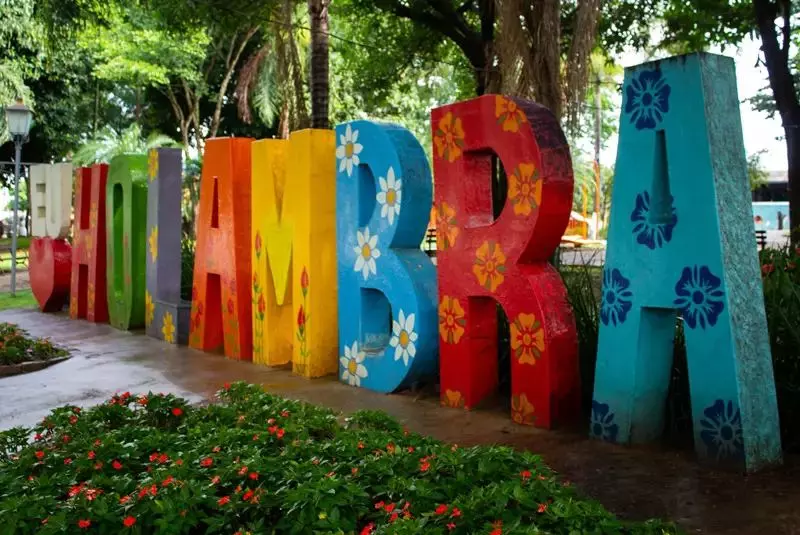 Letreiro escrito 'eu amo Holambra" com diferentes cores em um praça florida.