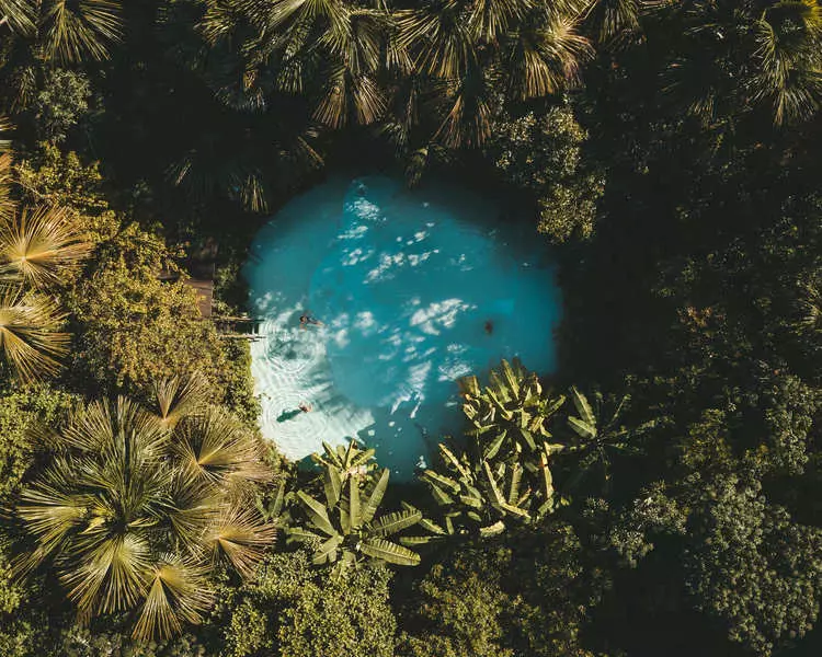 Um fervedouro de água cristalina e aspecto azulado com algumas pessoas dentro certados por floresta no parque estadual do Jalapão.