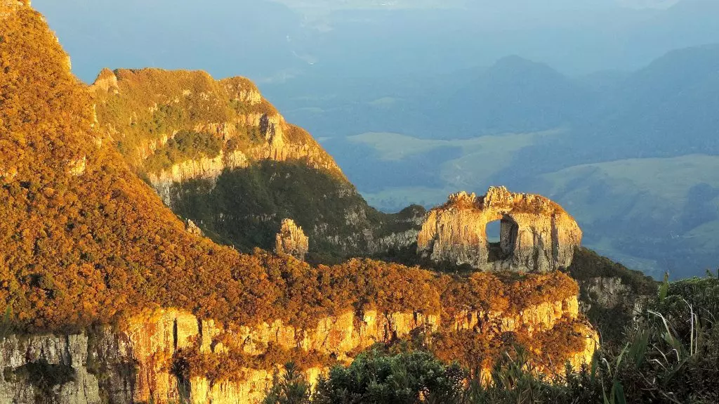 Montanha rochosa com cobertura baixa de vegetação com a pedra furada, monólito natural de pedra com um buraco em seu centro, nas serras de Urubici.