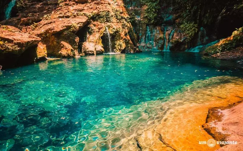 Parque Nacional da Chapada das Mesas, em Carolina Maranhão. Piscina natural de águas azuladas cristalinas cercada por rochas amareladas com pétalas de flores boiando sobre a água.