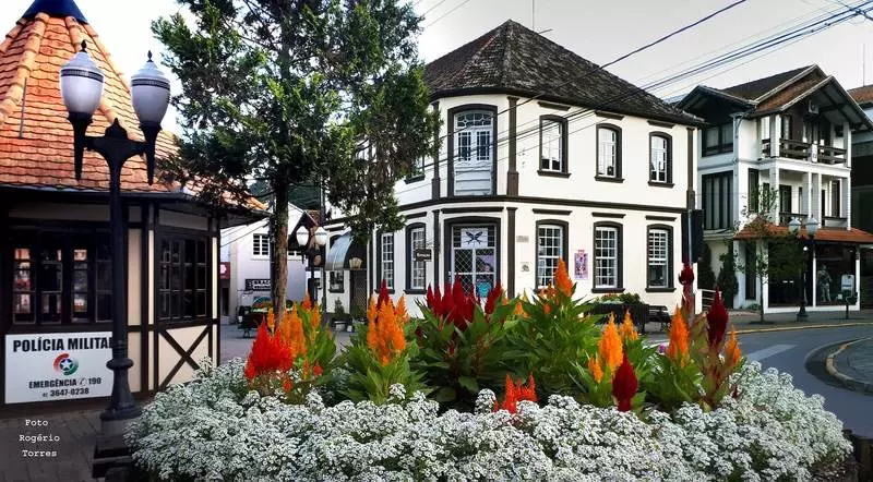 Cruzamento em São Bento do Sul com um jardim de flores locais, com uma casa com estilo colonial ao fundo ao lado de um postinho policial.