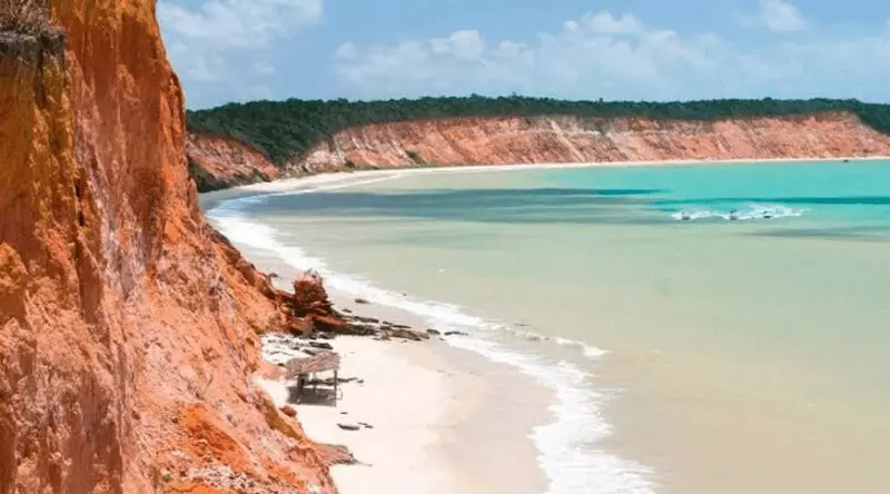 Falésias terrosas separadas da água em tons cristalinos de verde, por uma fina camada de areia branca, num das melhores praias do Espírito Santo.